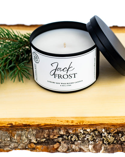 Soy Wax Candles - 6oz Jack Frost candle with lid and green pine branch on a wooden surface.