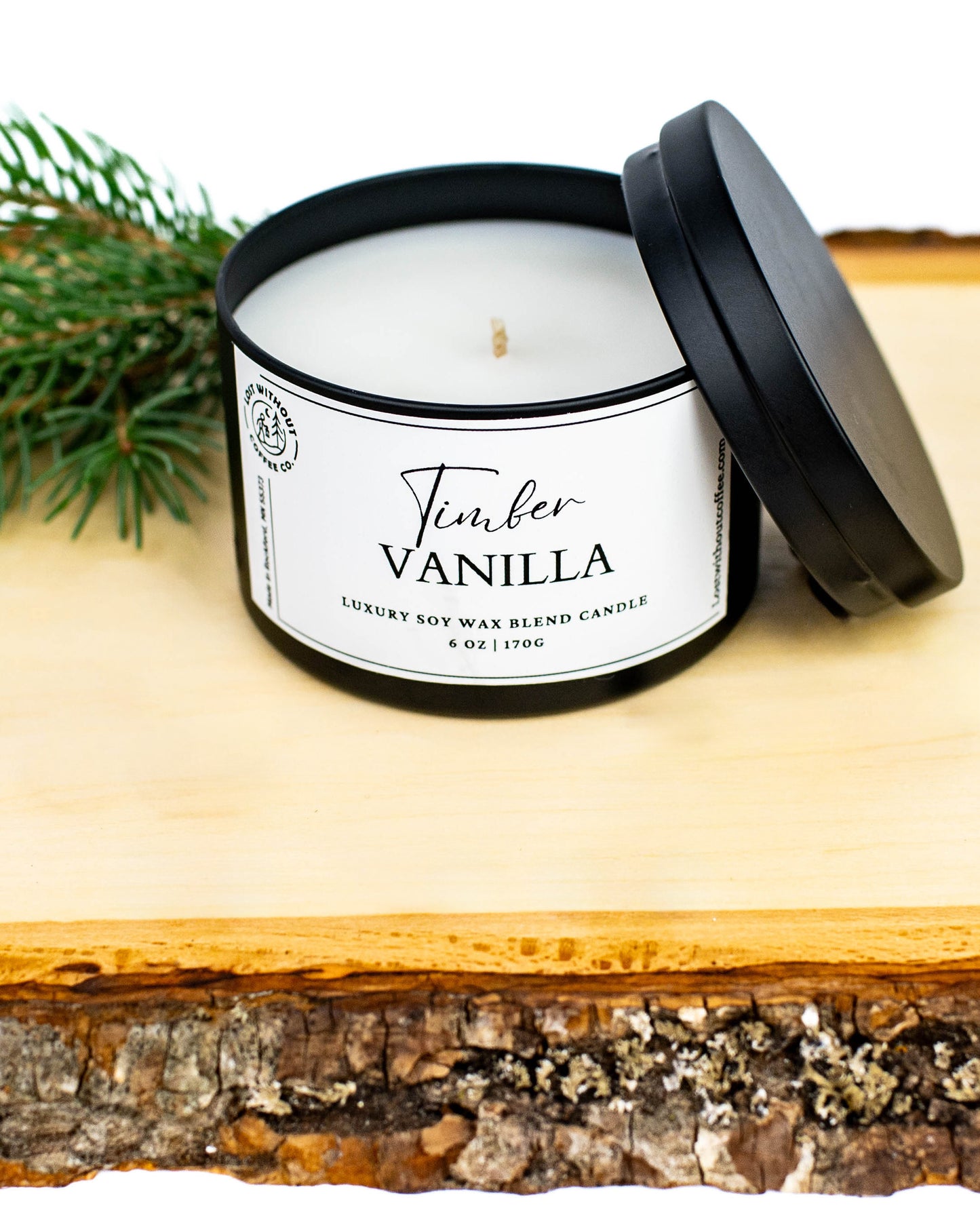 Timber Vanilla 6oz soy wax candles in a black container on a wooden surface with greenery background