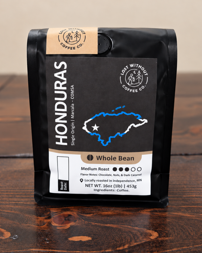 A 16oz black stand-up pouch of Honduras Whole Bean coffee from Lose Without Coffee Co., placed on a dark wooden table against a neutral beige background.