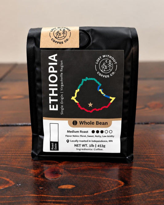 A black bag of Cat Without Coffee Co. Ethiopia whole bean coffee sits on a dark wooden table against a neutral beige background.